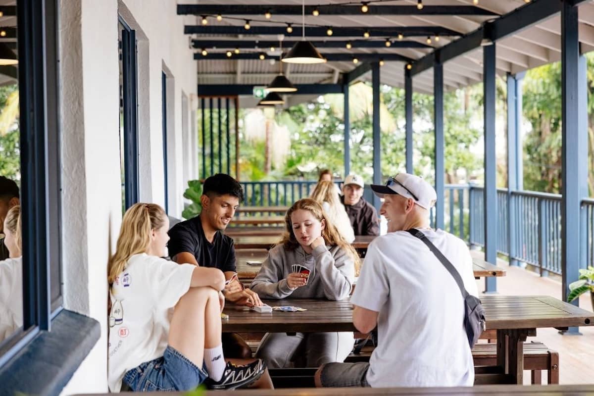 Group of travellers socialising and playing cards on a veranda at YHA Byron Bay.
