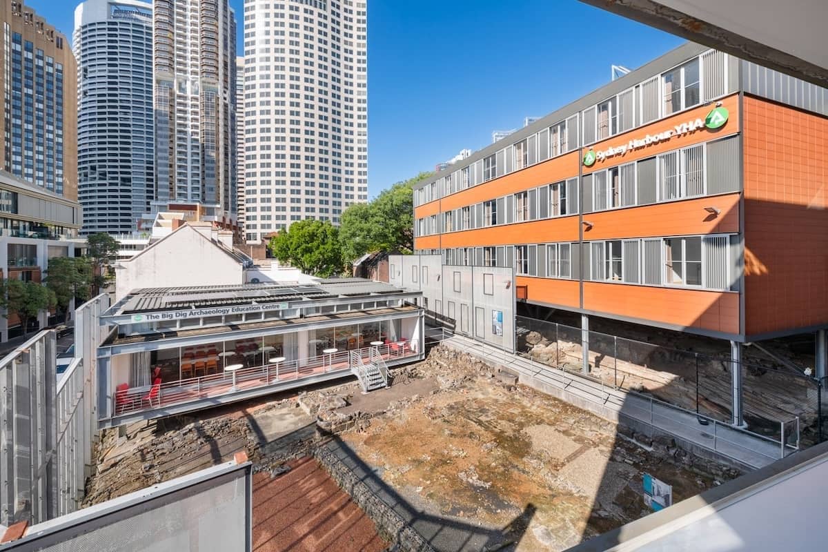 Sydney Harbour YHA next to the Big Dig archaeological site with city buildings in the background.
