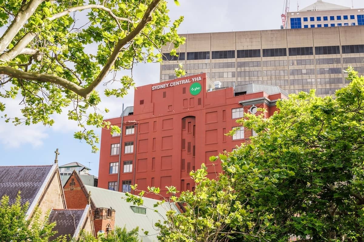 Sydney Central YHA building with leafy trees in the foreground and city buildings behind.